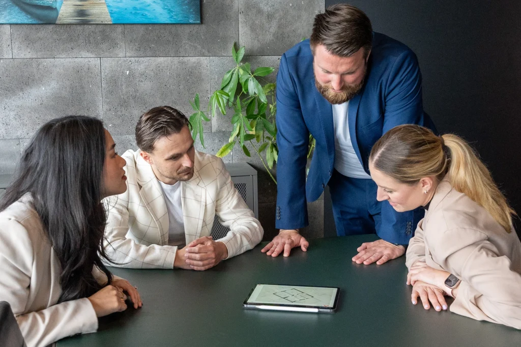 Zwei Frauen und zwei Männer in Business-Kleidung betrachten konzentriert einen Grundriss auf einem Tablet, passend zum Thema André Lautermann Immobilien Beratung und Wertermittlung.